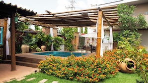 A garden with a pool, surrounded by a wooden pergola, and a variety of plants and flowers.