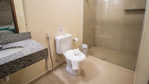 A bathroom with a granite countertop, a toilet, a glass-enclosed shower, and a visible trash bin.