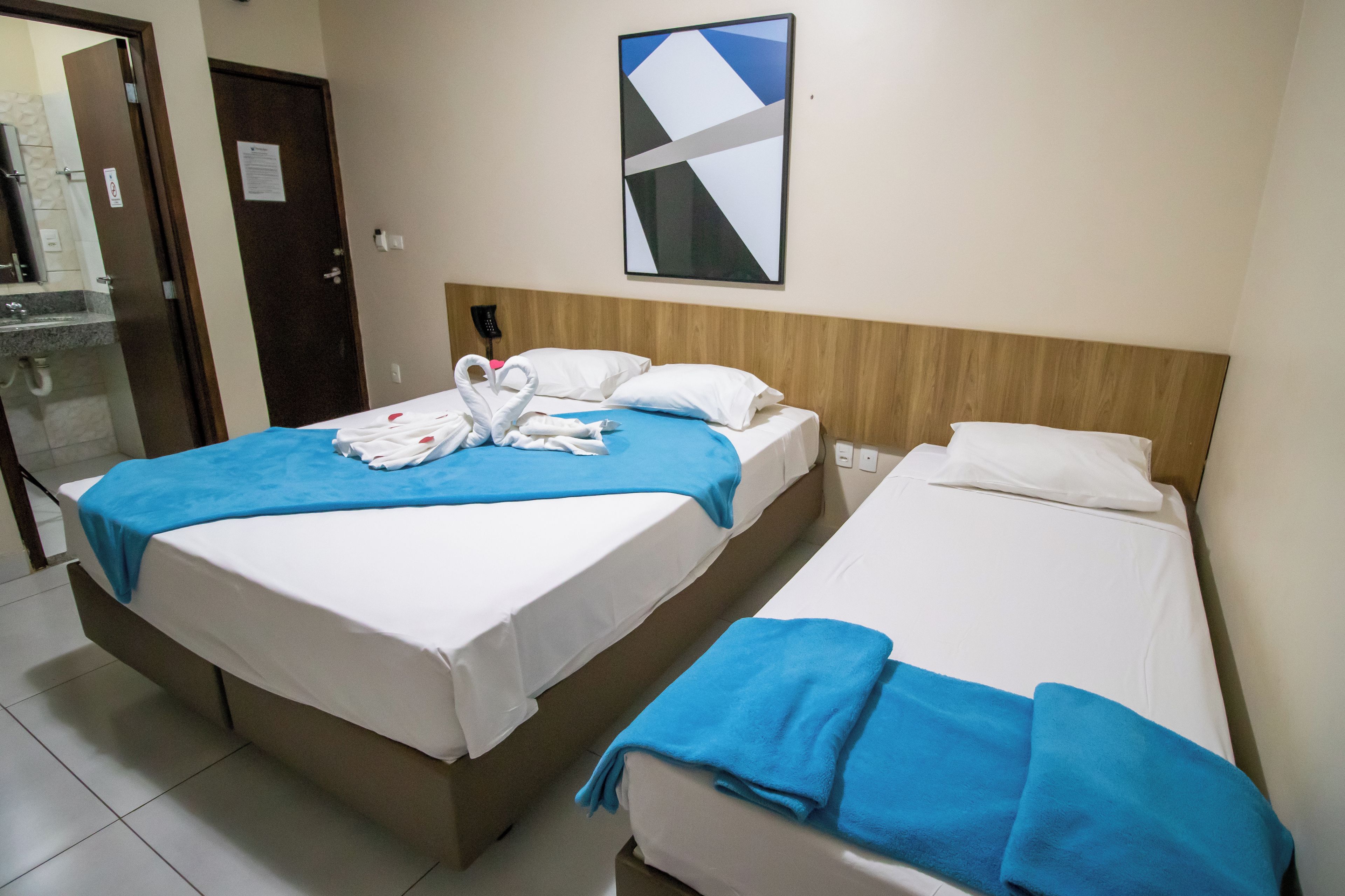 Habitación de hotel con dos camas, una más grande y otra más pequeña. Hay una obra de arte colgada en la pared sobre la cama más grande.