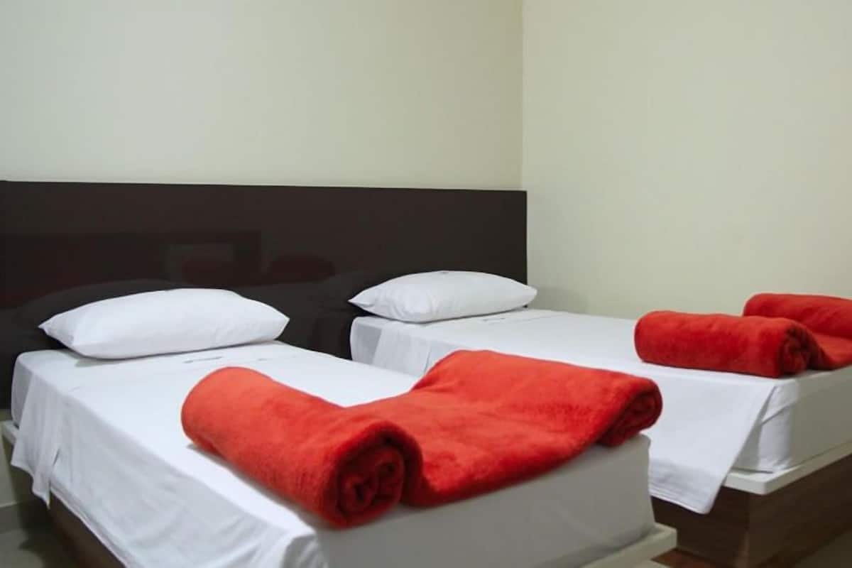 A hotel room with two single beds, each with a white bedspread and a red towel.
