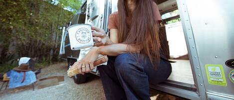A person sitting in a vehicle with a can of 'Caravan Outpost' and a bottle.