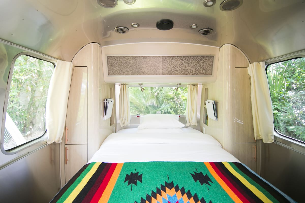 A narrow, single-bed RV with a window on one side, a small kitchenette, and a ceiling with ventilation.