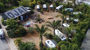 Vue aérienne d’un terrain de camping avec des véhicules récréatifs, un petit bâtiment portant l’inscription « AJAI » et une végétation luxuriante tout autour.