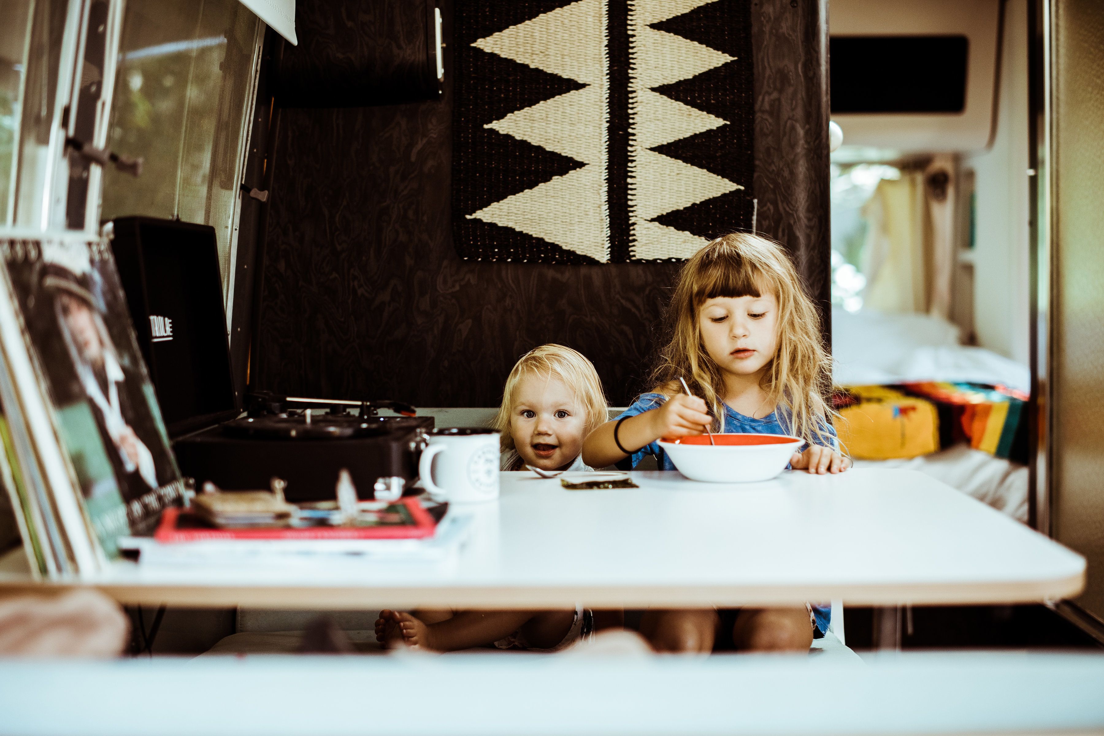 A dining area with a table, chairs, and a child eating. There is a wall with a geometric pattern and a window.