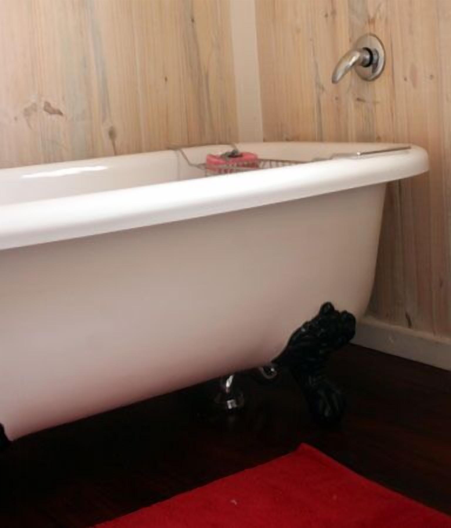 A white bathtub with claw feet in a bathroom with wooden walls.