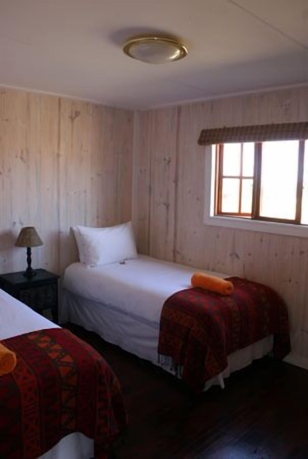 A room with two single beds, a nightstand with a lamp, and a window with a view.