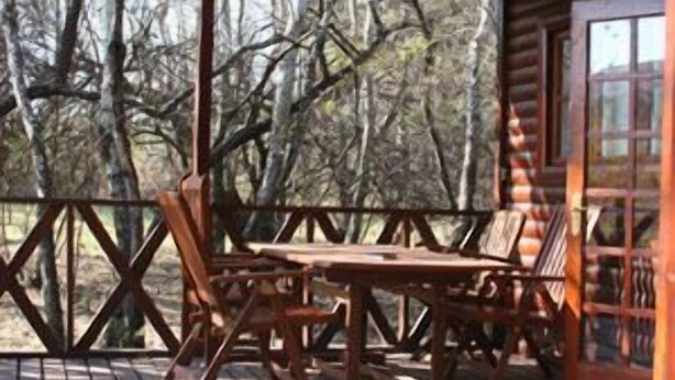 Una terraza de madera con una mesa y sillas, rodeada por una valla de madera y árboles.