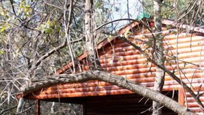 Una cabaña de madera con un porche y sillas, rodeada de árboles.