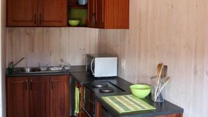 Cocina compacta con armarios de madera, microondas y una pequeña isla con tabla de cortar.