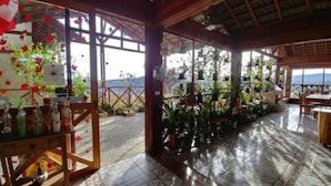 Ein überdachter Patio-Bereich mit Blick auf das Meer, Holzmöbel und Blumentöpfe.
