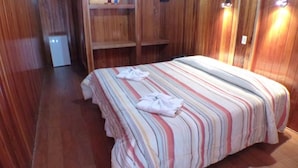 Ein Zimmer mit Holzwänden, einem Bett, einem kleinen Schreibtisch und einem Regal mit Gegenständen.