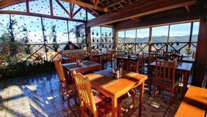 Ein Restaurant im Freien mit Holztischen und -stühlen, großen Fenstern und Blick auf die Berge.