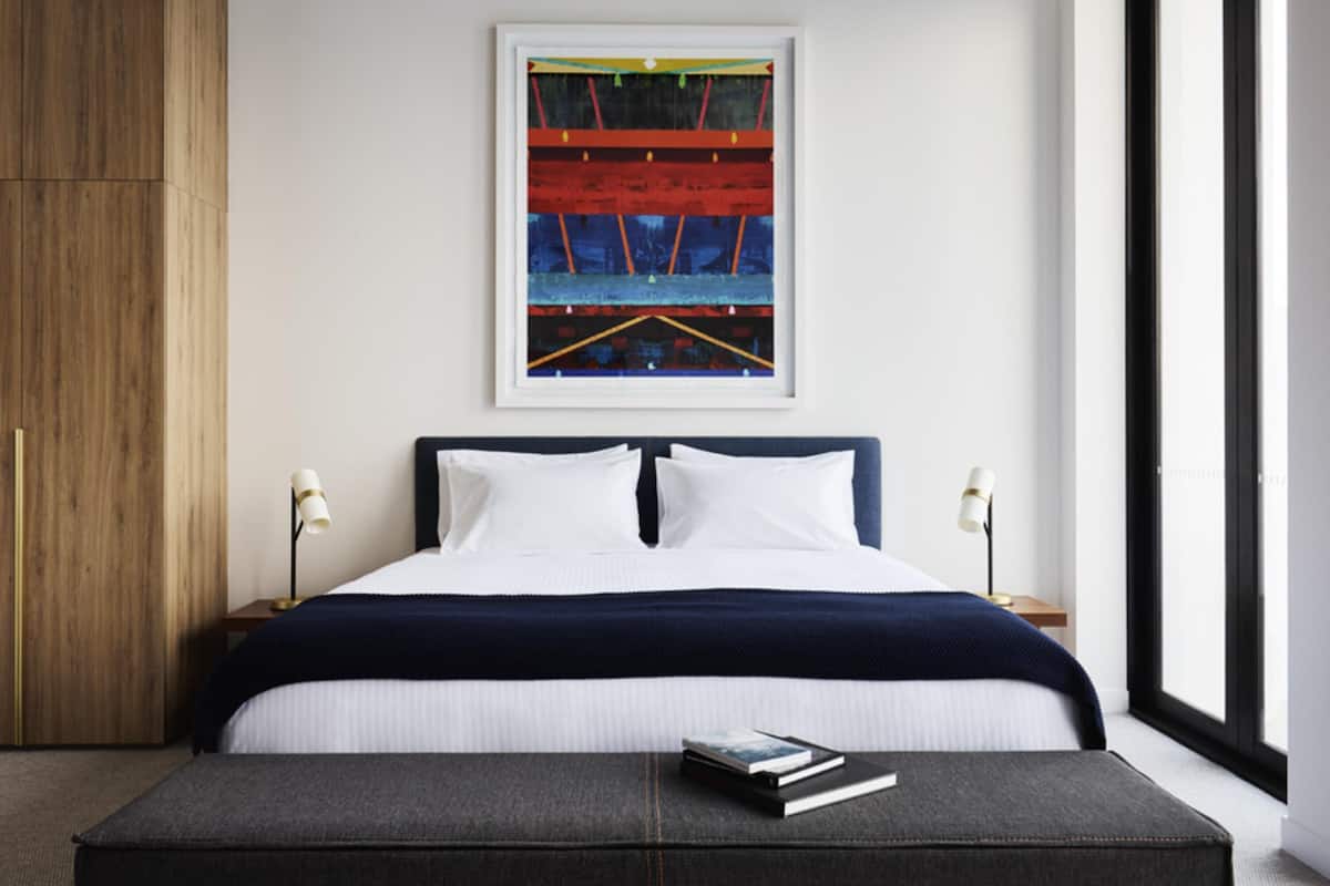 Un dormitorio moderno con una cama grande, un cuadro abstracto enmarco y una mesita de noche con lámpara.