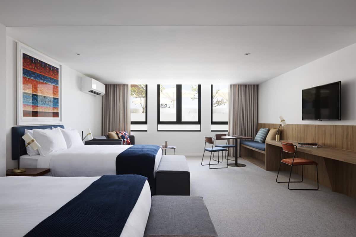 Una habitación de hotel con dos camas, un escritorio, una silla, un televisor y ventanas amplias.