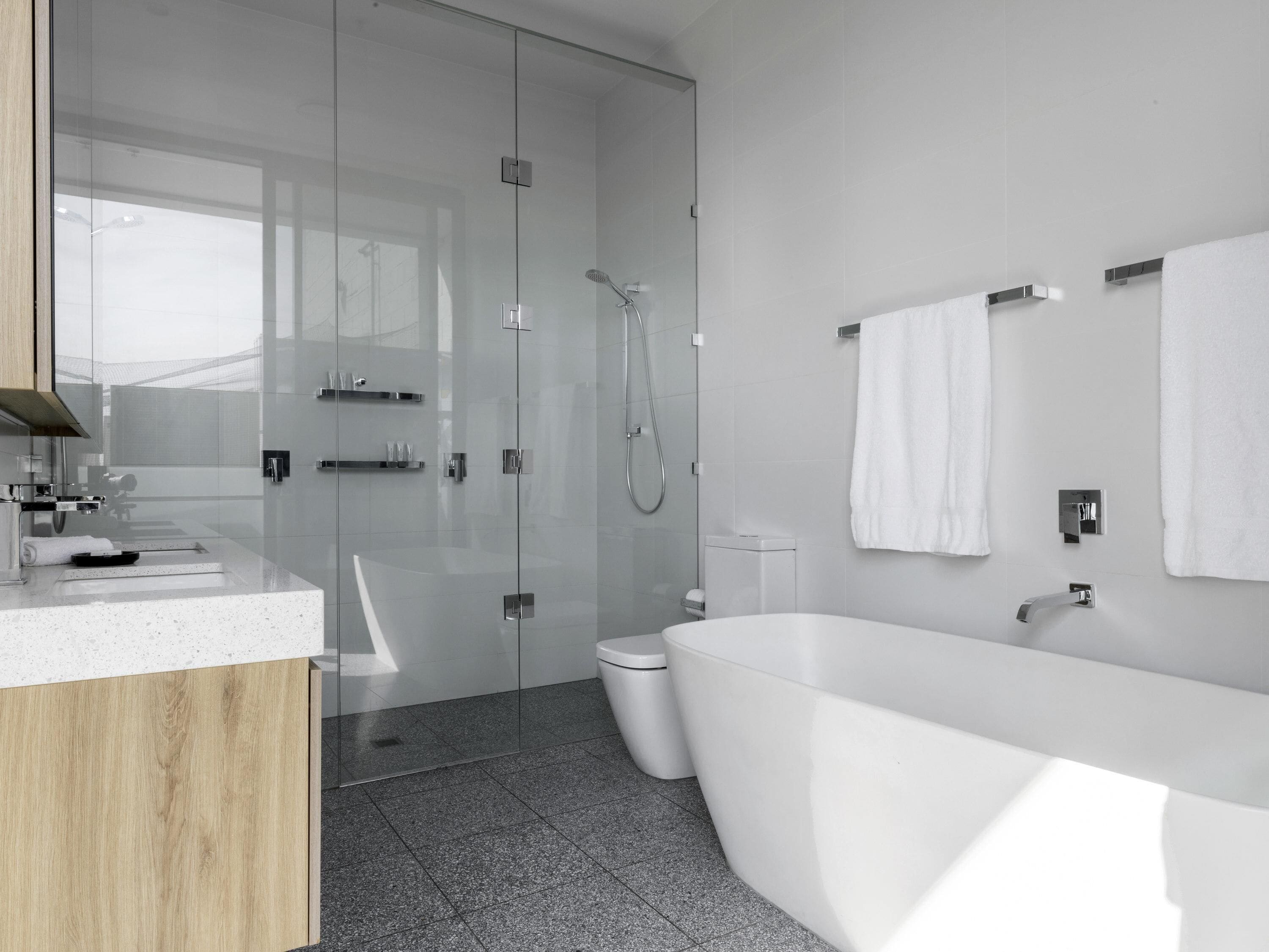 Ein modernes Badezimmer mit einer Glaskabine, einer freistehenden Badewanne und einem WC.