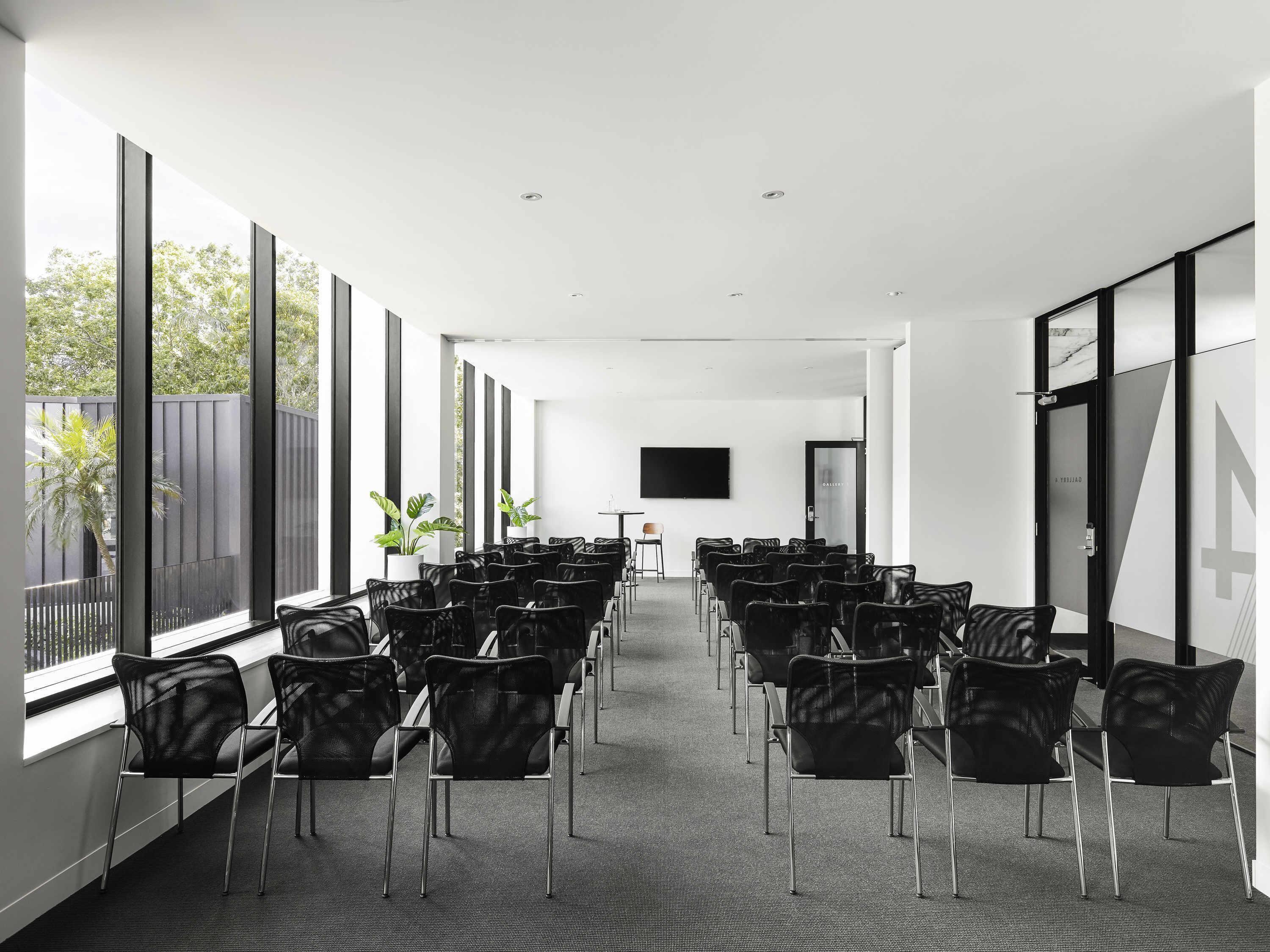 A conference room with rows of chairs, large windows, and a flat-screen TV.