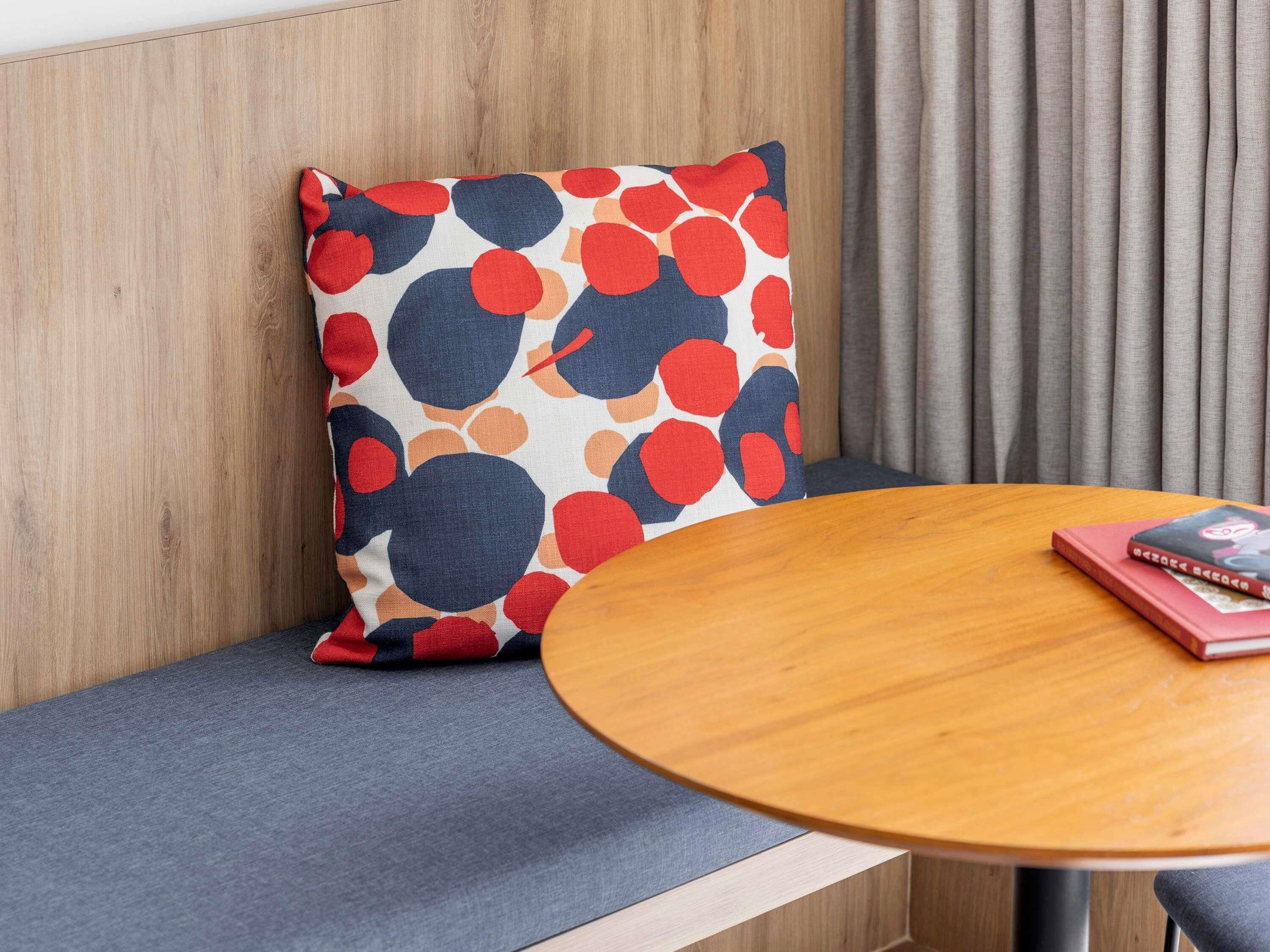 A seating area with a round wooden table, a cushion with a polka dot pattern, and a book on the table.