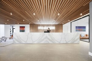 A modern reception area with a marble counter, wooden slatted ceiling, and artwork on the walls.