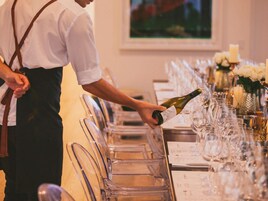 A waiter pouring wine into glasses at a table set for a meal.