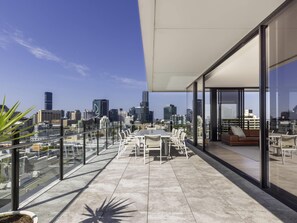 Une terrasse moderne sur le toit, offrant une vue panoramique sur la ville, avec un espace repas doté de mobilier blanc et un coin salon avec un canapé et des fauteuils.