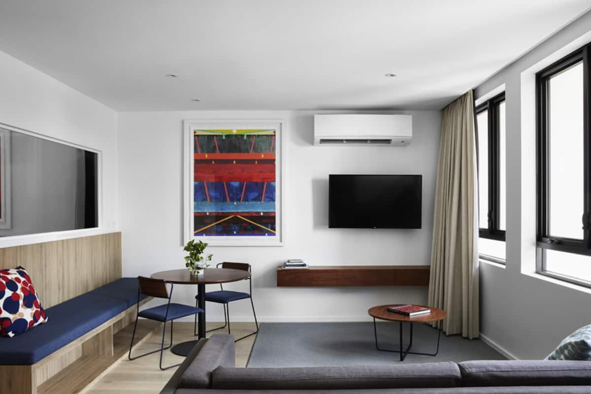 Una sala de estar moderna con un sofá, una mesa de comedor con sillas, un televisor de pantalla plana y un ventanal grande.