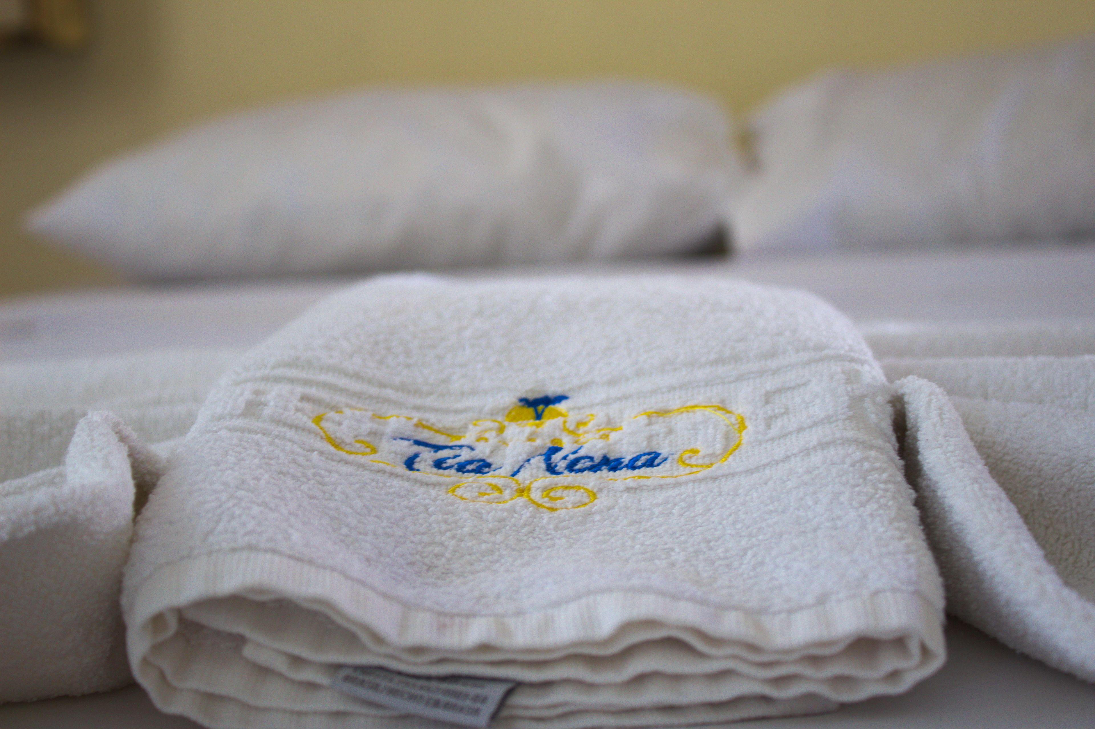 A stack of white towels with embroidered text and a logo on a bed.
