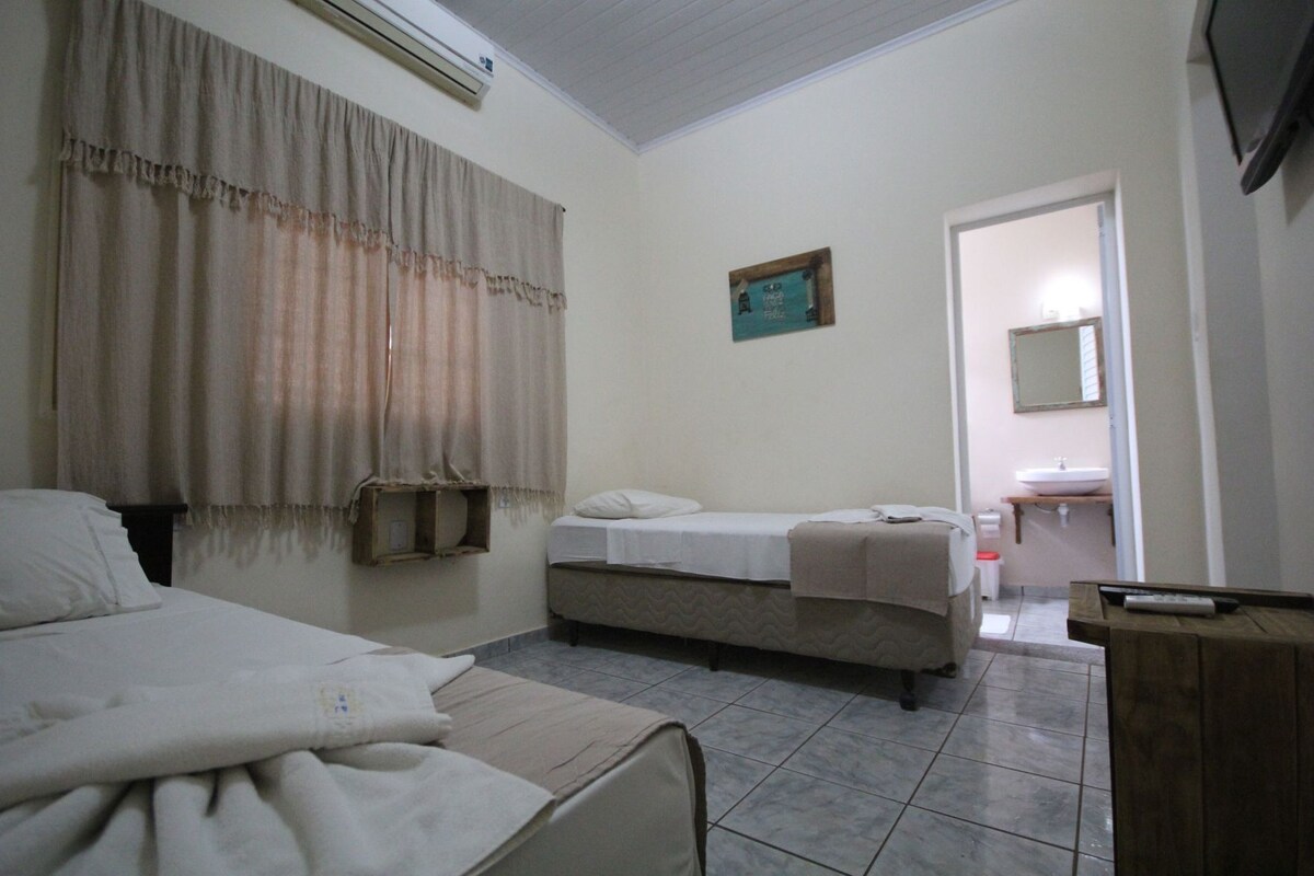 Un dormitorio con dos camas, una mesita de noche, un espejo, un estante pequeño y un baño con lavamanos y espejo.