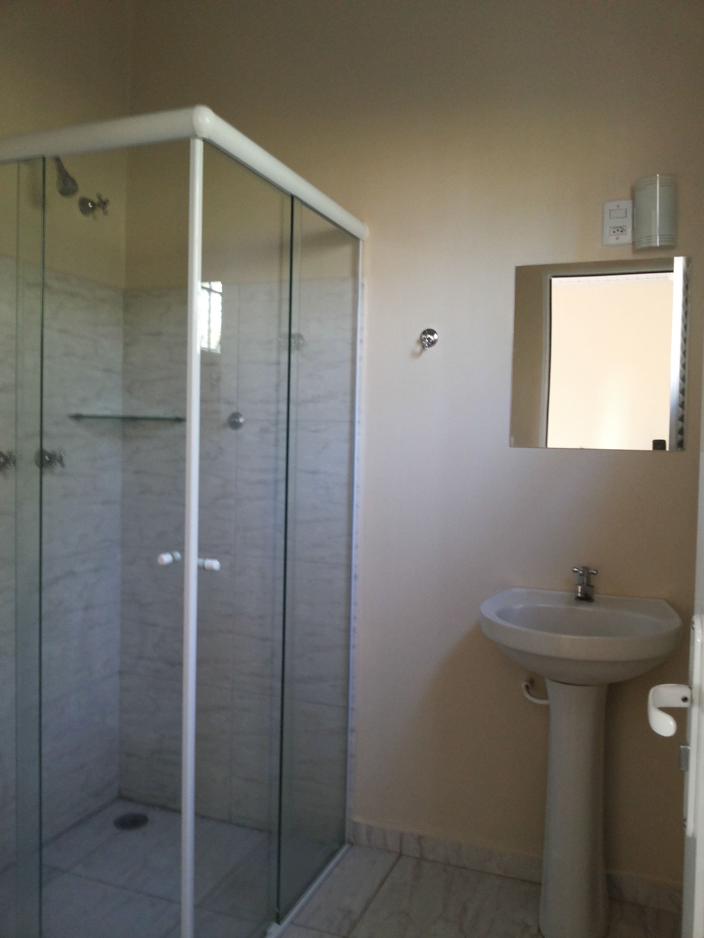 A bathroom with a glass-enclosed shower, a pedestal sink, and a mirror above the sink.