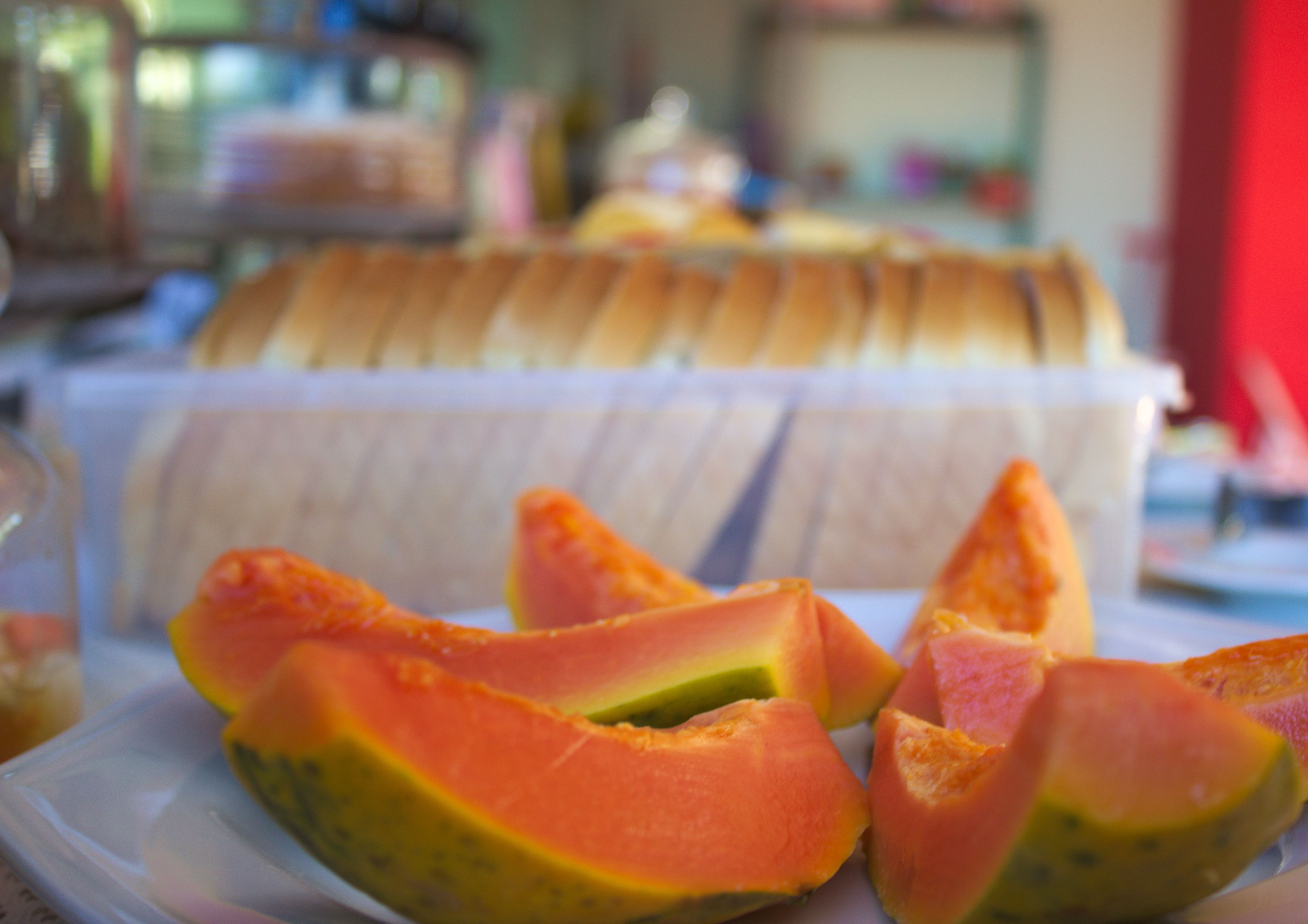 Un plato de papaya en rodajas y un recipiente blanco con pan.