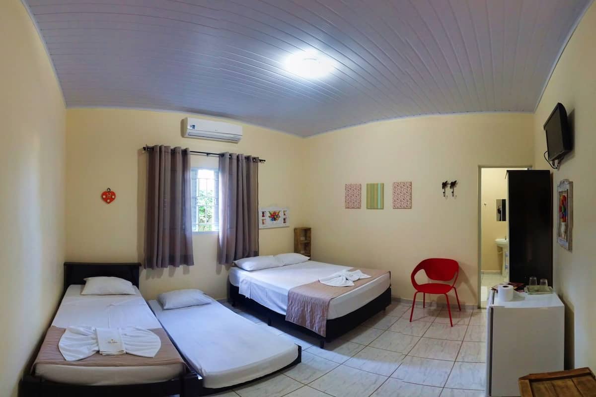 Une chambre avec trois lits simples, un fauteuil rouge, une télévision et un réfrigérateur.