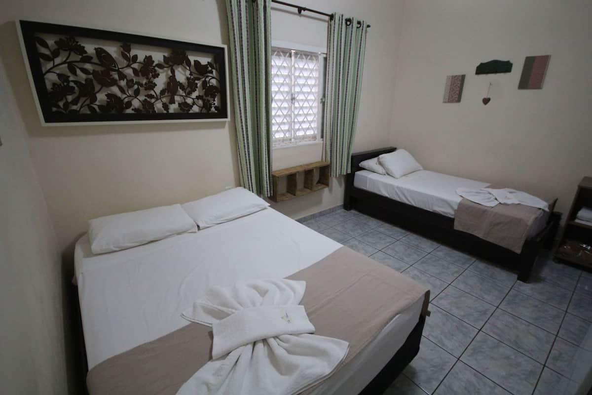 Une chambre d’hôtel avec un grand lit, un plus petit lit, une fenêtre avec des rideaux, un élément de décoration murale et une table de chevet.