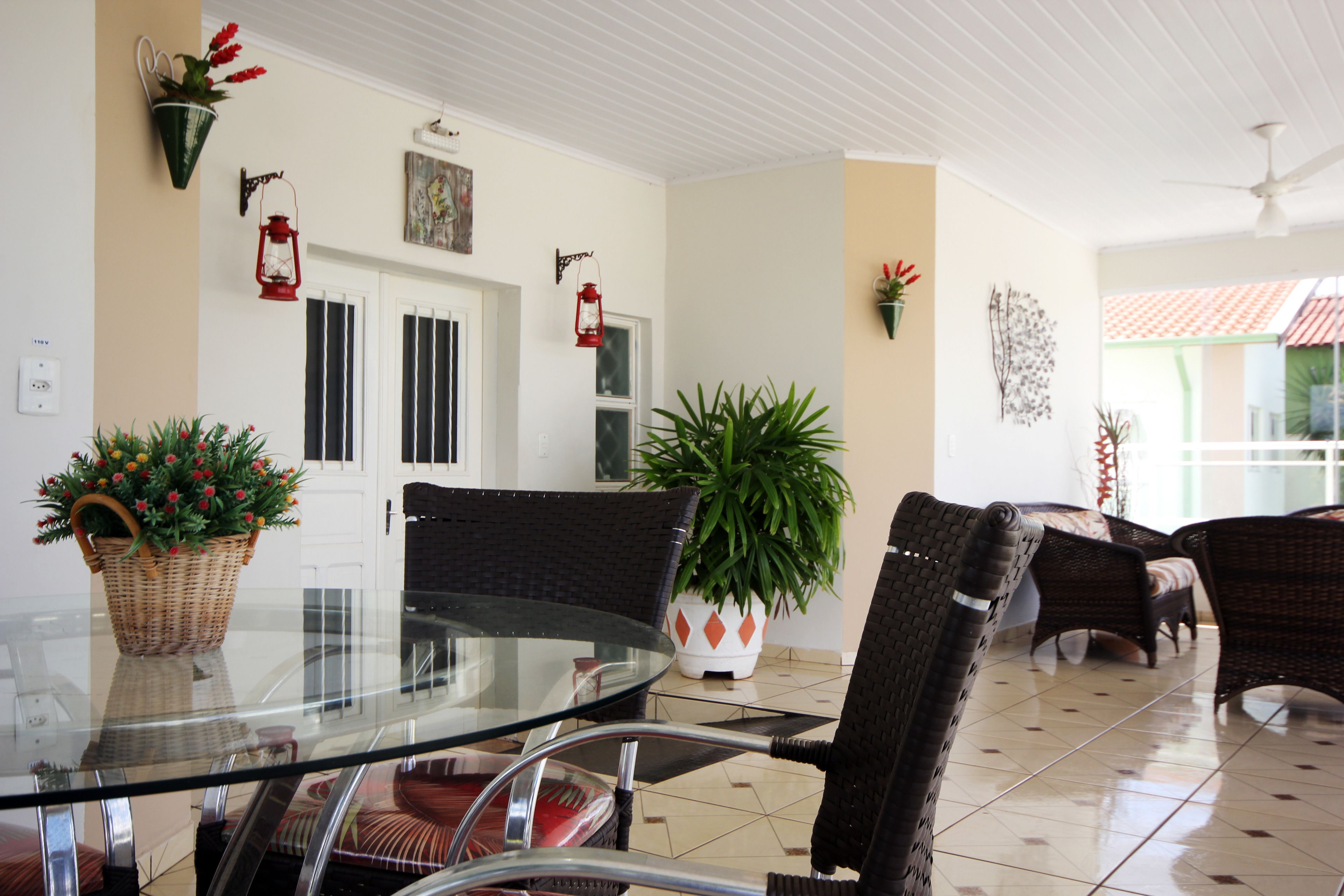 A dining area with a glass table, wicker chairs, potted plants, and a white door.