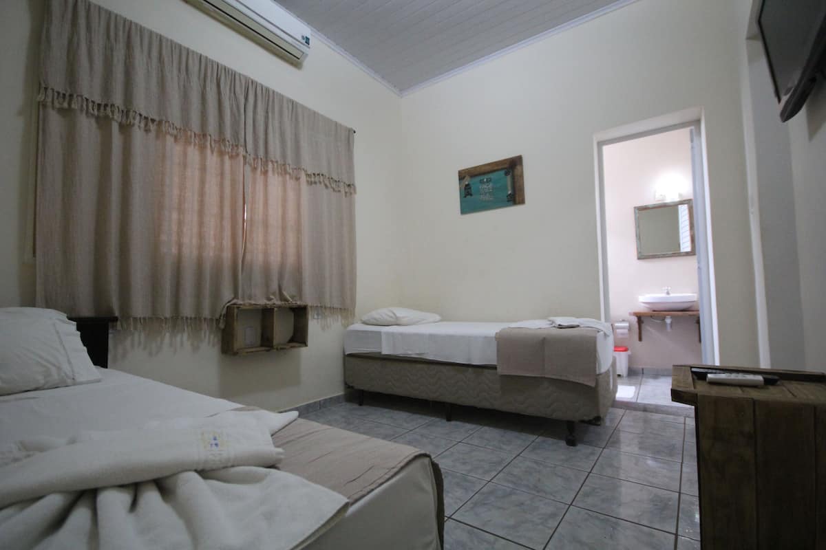 Une chambre avec deux lits, une table de chevet, un miroir et une salle de bain visible à travers une porte ouverte.