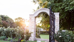 A stone archway with a checkered path leading through it, surrounded by lush greenery and flowering plants.