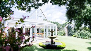 A conservatory with a fountain, surrounded by a well-maintained lawn and garden.