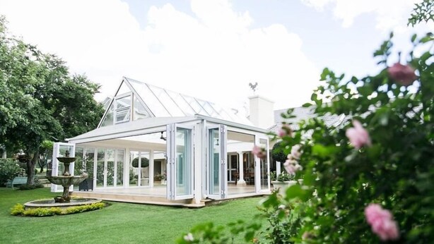 A modern glass conservatory with a lawn and fountain.