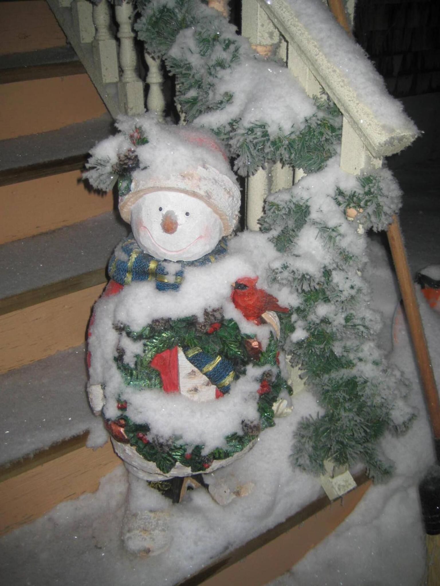 A snowman with a hat and scarf, positioned next to a staircase and a small Christmas tree.