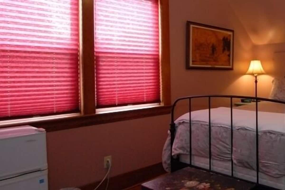 A bedroom with a single bed, two bedside lamps, a nightstand, and a window with blinds.