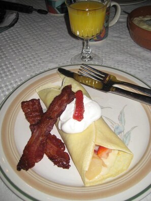 A plate with a crepe, strawberries, and bacon.