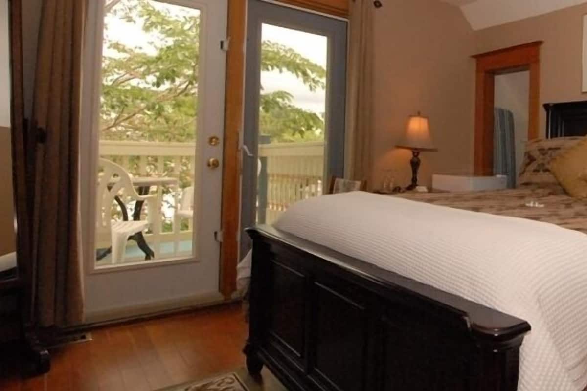 A bedroom with a bed, two bedside tables with lamps, a dresser, and a sliding glass door leading to an outdoor area.