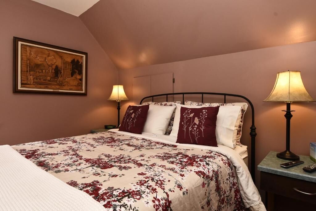 Ein Schlafzimmer mit einem Bett, zwei Nachttischlampen, einem Nachttisch und einem gerahmten Bild an der Wand.