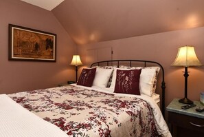 A bedroom with a bed, two bedside lamps, a nightstand, and a framed picture on the wall.