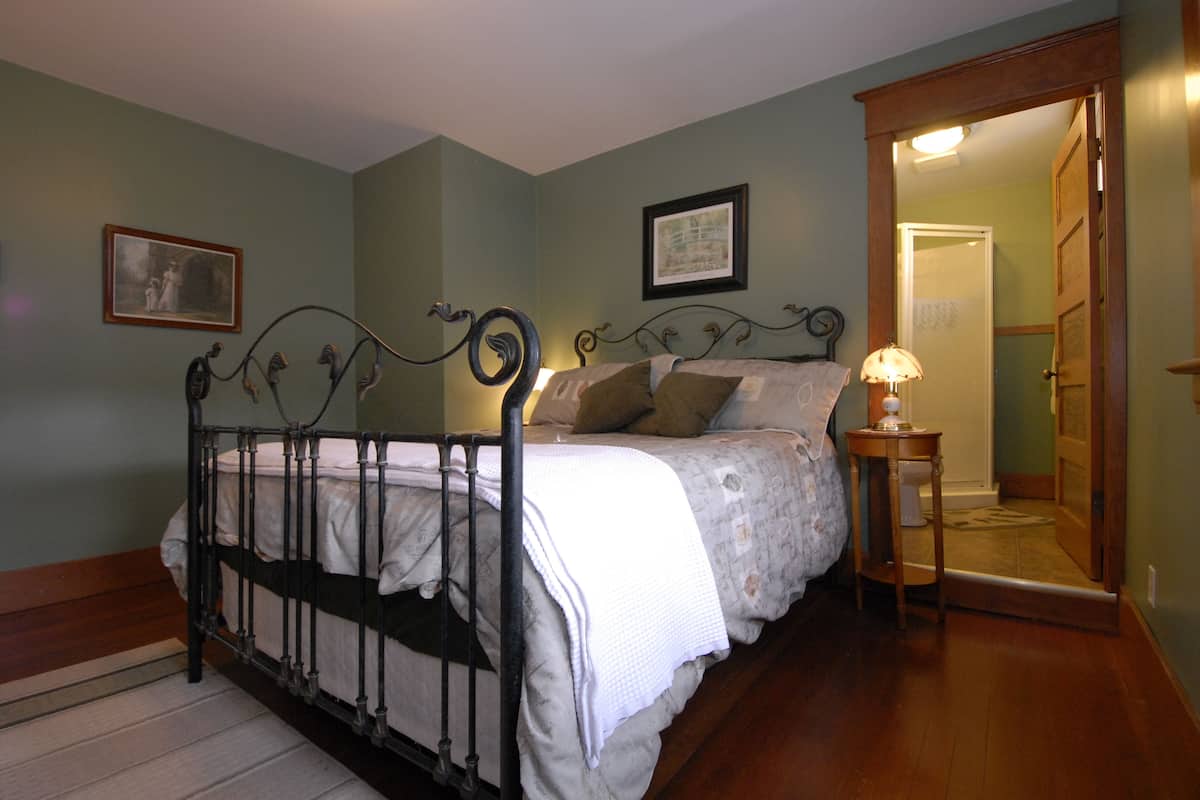 A bedroom with a metal bed frame, a bedside table with a lamp, and a door leading to another room.