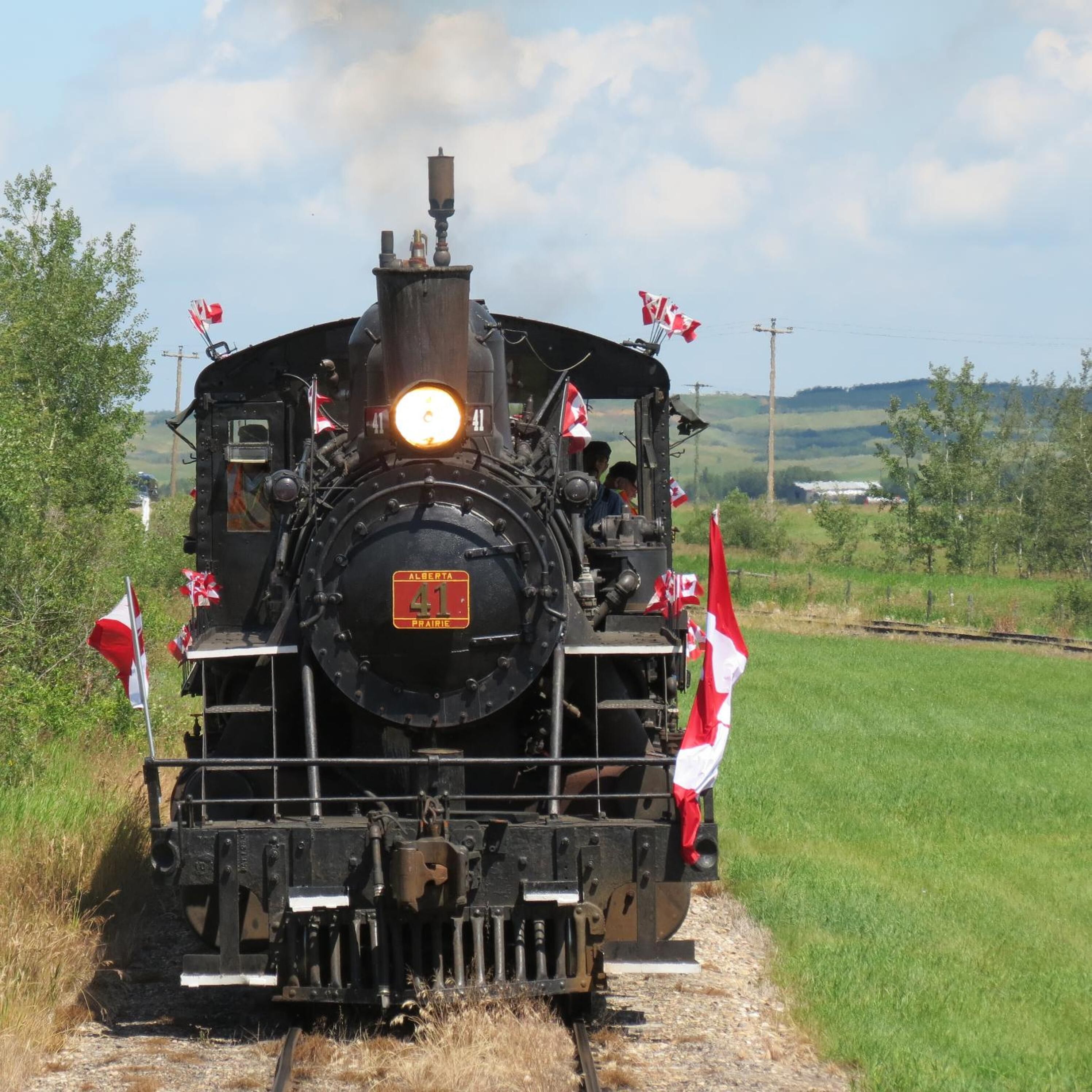 A steam locomotive with the number 41, adorned with Canadian flags, traveling on a railway track surrounded by greenery.