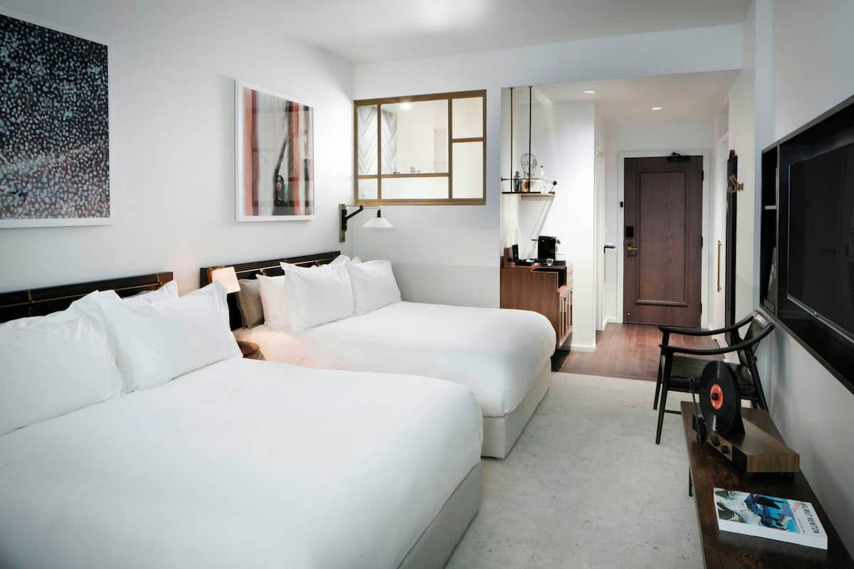 A hotel room with two beds, a TV, a coffee machine, and a desk with a chair.