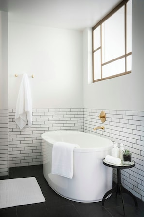 Un baño moderno con una bañera independiente, una mesita con artículos de aseo, y un ventanal que proporciona luz natural.