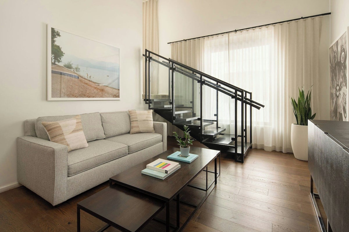 A living room with a sofa, coffee table, and a staircase with glass railings.