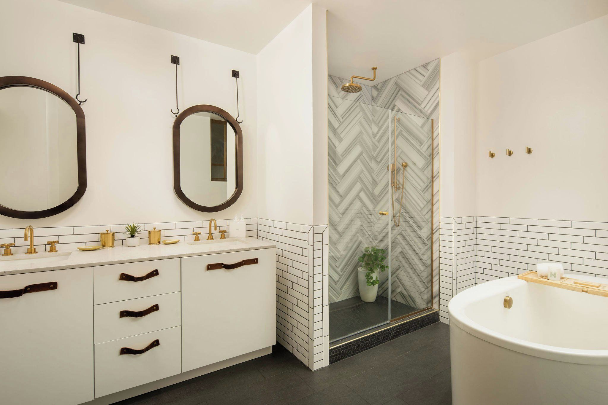 Un baño moderno con tocador blanco, detalles dorados, un espejo grande y una ducha con diseño de espiga.