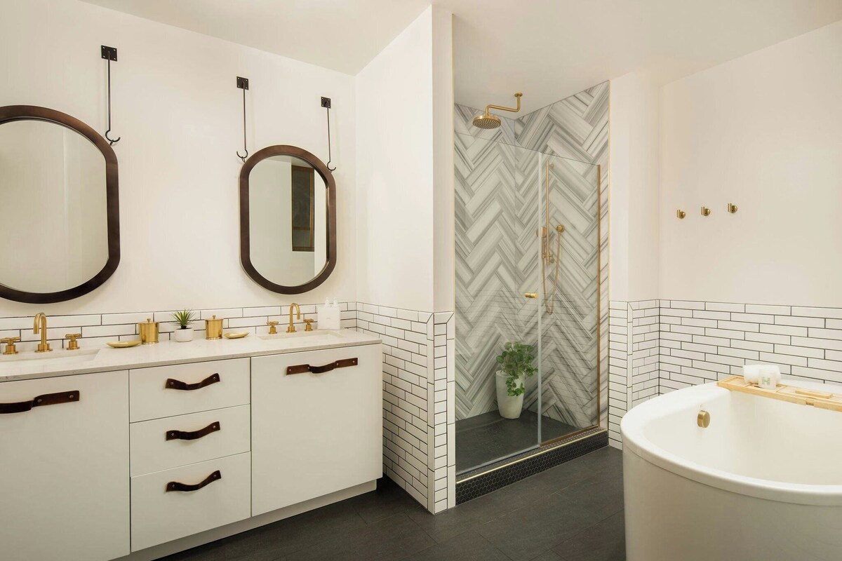 Un baño moderno con un espejo grande, dos lavamanos, una bañera y una ducha con un diseño de baldosas en espiga.