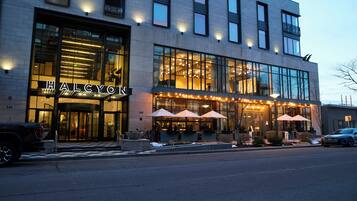 A modern building with a glass facade, outdoor seating area, and a sign reading 'ALCYON'.